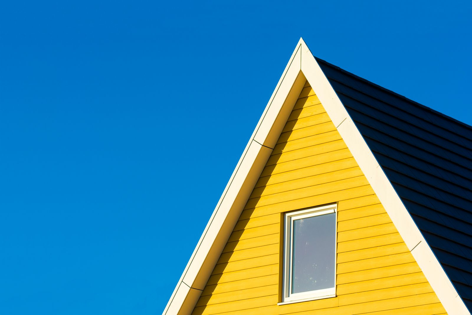Close-up of a yellow house with a triangle roof against a clear blue sky.